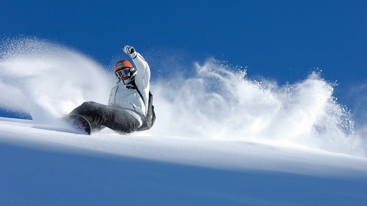 Snowboard kenar kontrolü sırasında kar savuran sporcu.